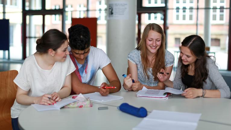 Vier Schüler*innen sitzen an einem Tisch und lernen gemeinsam